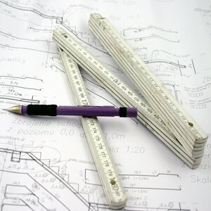 Picture of construction draft papers, a pencil, and a ruler/measuring tape.