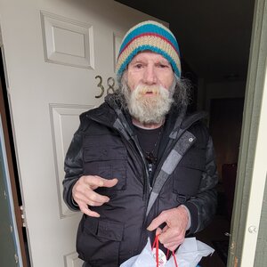 Picture of an elderly man standing in his doorway with a winter coat and hat on.